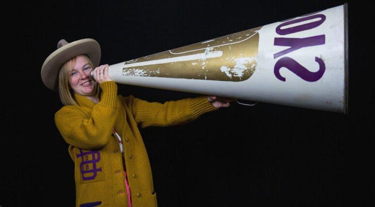 A student dressed in historic cheer outfit with giant megaphone.